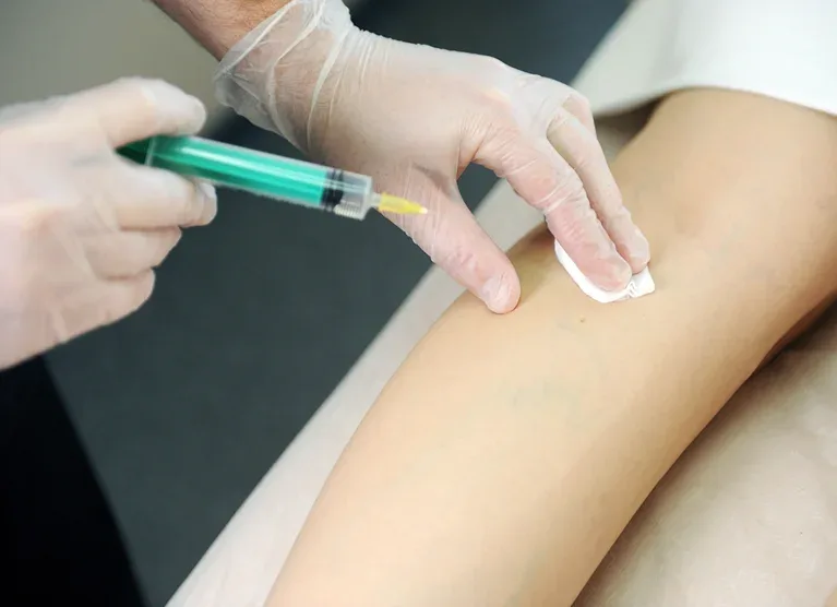 Gloved hand holding an injection with another hand pressing a cotton to the portion of the leg that has been injected.